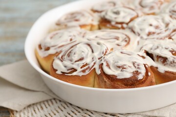 Delicious frosted cinnamon rolls in baking dish on table, closeup