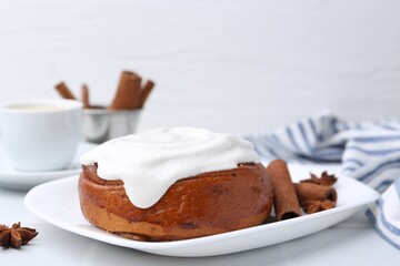 Tasty cinnamon roll with cream and spices on white table, closeup. Space for text