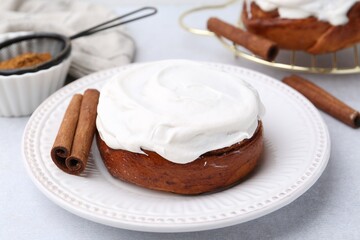 Tasty cinnamon roll with cream and spices on light table, closeup