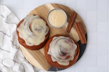 Tasty cinnamon rolls with cream and spices on white tiled table, top view
