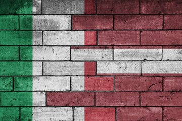 colourful painted big flag of italy and flag of latvia on a massive old brick wall background....