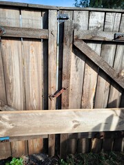 Old wooden door closed with an old lock. Wooden fence gate. Wooden fence with a rusty nail in the garden on a sunny day