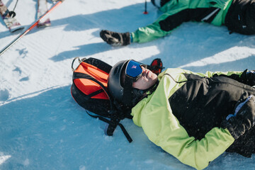 A skier relaxes on the snowy ground during a skiing activity, showcasing winter leisurewear and...