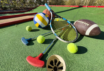 A variety of sports equipment including an american football, a soccer ball, a tennis racket, a tennis ball, and a basketball