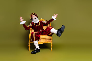 Elderly nobleman in regal attire sitting on a vintage armchair over a khaki background