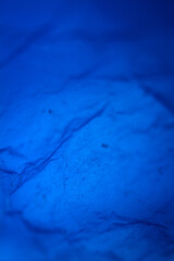 Extreme close up of blue empty plastic bag background. The plastic surface is wrinkly and tattered making abstract pattern. Selective focus, shallow depth of field.