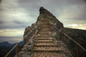 A stone staircase ascends a rugged mountain peak under an overcast sky, offering breathtaking views...
