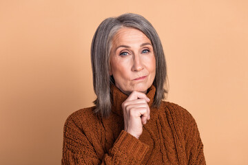 Charming elderly woman in a cozy brown sweater posing confidently against a beige background
