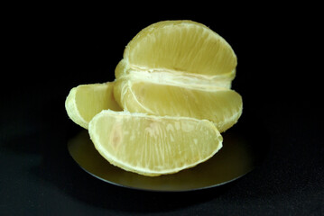 half of a peeled lemon with separate slices on a black plate in the dark