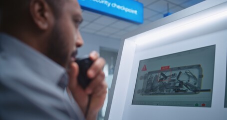Airport Terminal: African American Security Officer Monitors X-ray Luggage Scanning on Computer Screens, Finds Suspicious Item in Suitcase, Transmits Information by Walkie-Talkie. Security Checkpoint.