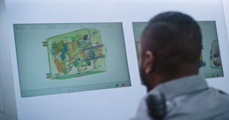 Airport Security Checkpoint: Back View of African American Security Officer Monitoring Baggage Screening on Computer. PC Screens Showing Modern Software for X-ray Scanning Technology for Plane Flight.