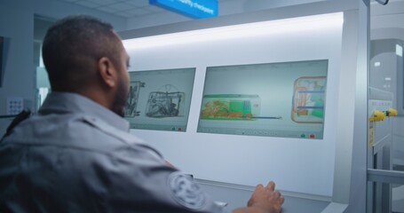 Airport Terminal: Back View of African American Security Officer Monitoring Baggage Screening...