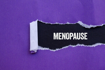 Menopause message written on ripped torn purple paper on black background. Conceptual menopause...