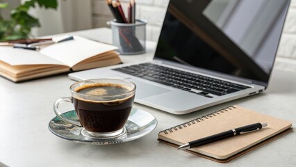A cup of coffee sits on a desk next to a laptop and open notebook, ready for a productive workday