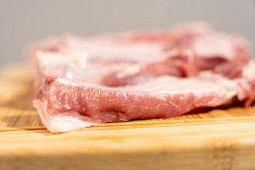 A piece of meat is on a wooden cutting board. The meat is cut into thin slices. The meat is white in color