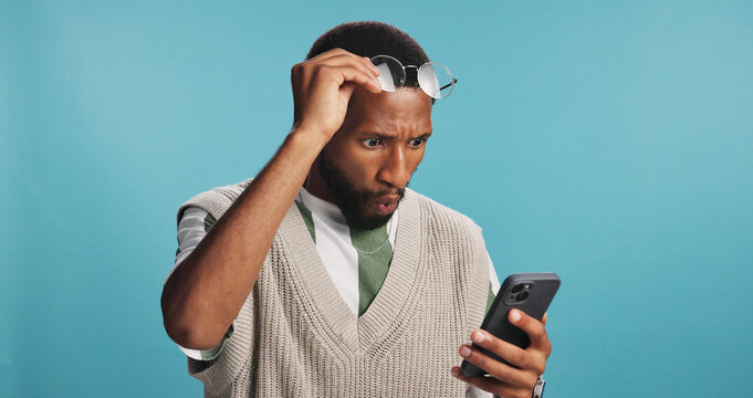 Surprise, shock and black man with phone for news, results or omg for college acceptance. Wow, mobile and person reading promo, unexpected notification or wtf emoji for win on blue studio background - Powered by Adobe