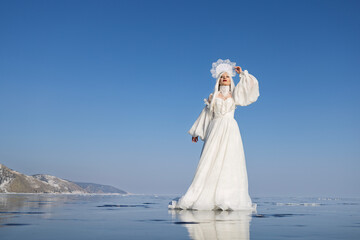 A woman in a white dress and traditional headdress on icy lake. Winter fairy tale, Snow Queen...