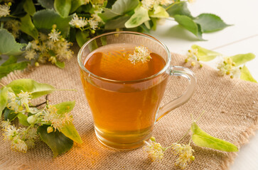 Herbal tea with lime blossom in a mug on a white wooden table with flowers
