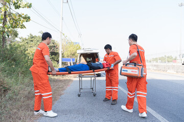 Injured man on patient transport stretcher. Ambulance staff member assisting injured person with transport stretcher. Paramedics assisting injured person first aid on road
