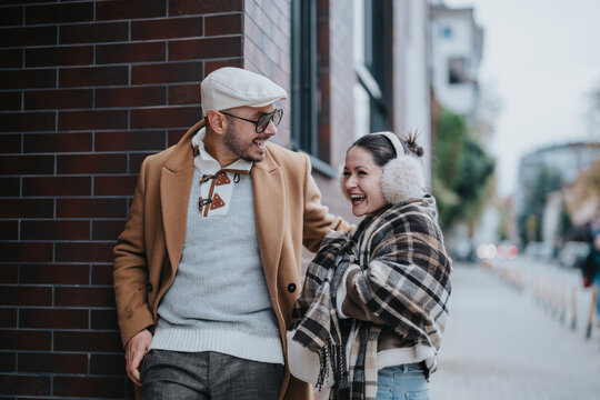 A joyful young couple enjoys a fun moment outdoors in stylish autumn attire. The setting creates a warm, urban ambiance, highlighting their happiness and connection in a vibrant city environment.