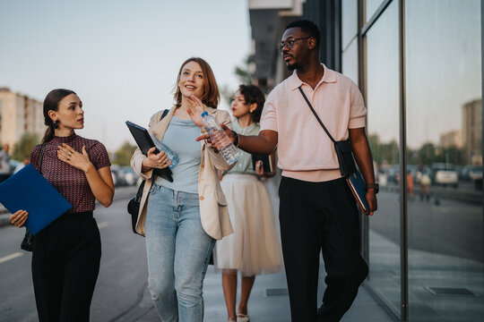A diverse group of business people walking and conversing outdoors, carrying folders and documents, suggesting a casual business meeting or discussion.