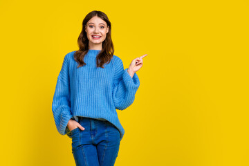 Cheerful young woman in a blue sweater against a vibrant yellow background expressing excited...