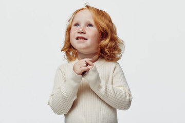 Little girl with red hair standing in front of white background with her hands on chest,...