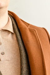 Detail of men casual outwear, fashionable mens brown coat combined with beige polo shirt and brown blazer. Selective focus.