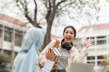 Diverse female student waving while holding books outdoors on campus.