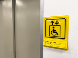Sign indicating elevator for people with disabilities. Yellow sign with wheelchair and braille text to indicate elevator for blind people. Creating living conditions for people with disabilities © malazoniia
