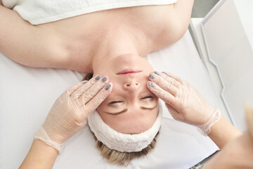 Caucasian female receiving relaxing facial massage at spa with closed eyes and headband.
