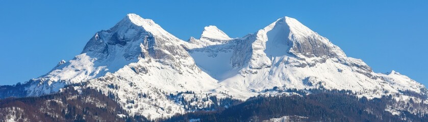 A panoramic view of majestic snow-capped mountains under a clear blue sky, showcasing the grandeur of nature and the beauty of winter landscapes.