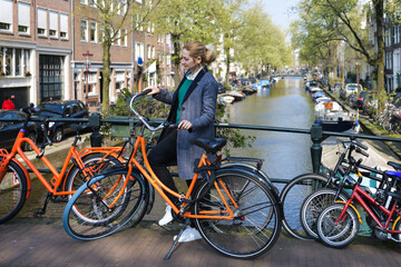 Beautiful blonde woman near the bicycle on the bridge over the water channel in Amsterdam old city