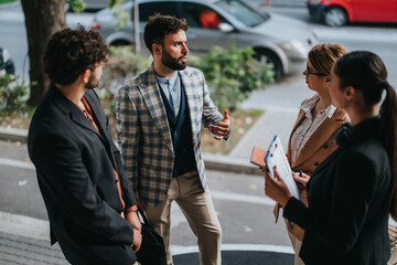 A group of business people discusses projects in an outdoor city setting. The atmosphere reflects...