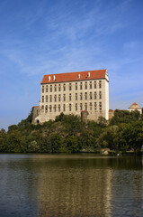 Obraz premium Photograph of a tall castle building on a rock above a pond. Monumental castle. Historic building, sky, monuments. The reflection of the castle on the surface of the pond. Travel, vacation. 