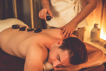 Hot stone massage at spa salon in luxury resort with warm candle light, blissful man customer...