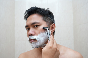 A man shaves his beard with foam and razor. Personal care and skin care concept.