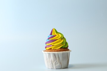 Tasty cupcake with colorful cream on light blue background