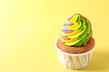 Tasty cupcake with colorful cream on yellow background, closeup. Space for text