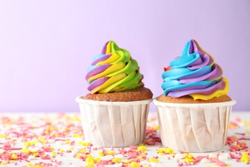 Delicious cupcakes with colorful cream and sprinkles on white wooden table against violet background, closeup. Space for text