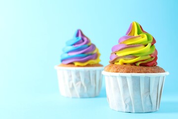 Delicious cupcakes with colorful cream on light blue background, closeup. Space for text