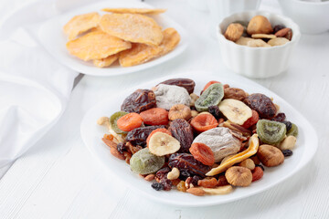 Mix of dried tropical fruits, nuts, and raisins on a white table.