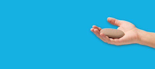 Hand holding stone on blue background with copy space.