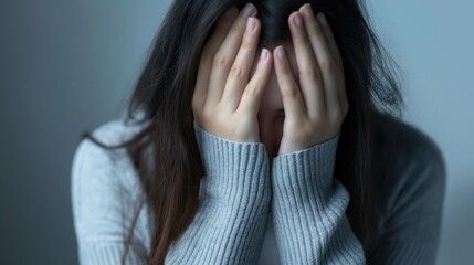 woman burying face in hands wearing cozy grey sweater indoors with moody lighting anxious feeling copyspace concept of mental health therapy counseling