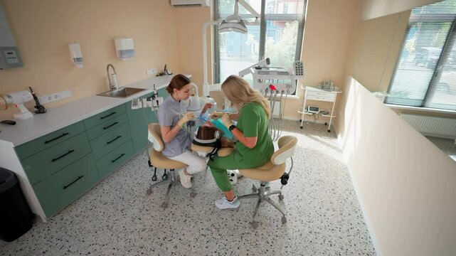 Blonde Woman Dentist with Assistant Treat Teeth of Female Patient with Special Instrument. Treatment of Caries and Plaque in Dental Clinic. Concept of Medicine and Healthcare. Slow Motion.