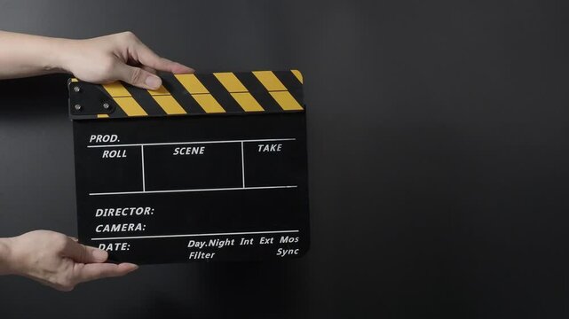 A classic film clapperboard or film slate being held and hit against a dark background. Symbolizes filmmaking video production movie filming and creative storytelling in the entertainment industry.