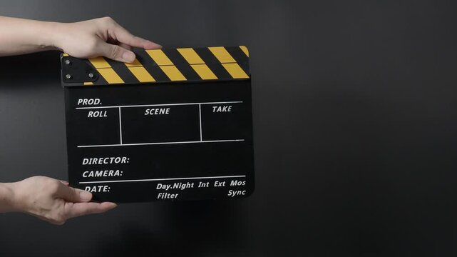 A classic film clapperboard or film slate being held and hit against a dark background. Symbolizes filmmaking video production movie filming and creative storytelling in the entertainment industry.