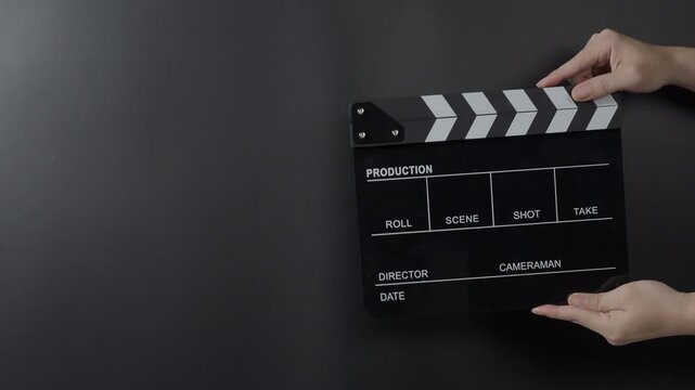 A classic film clapperboard or film slate being held and hit against a dark background. Symbolizes filmmaking video production movie filming and creative storytelling in the entertainment industry.