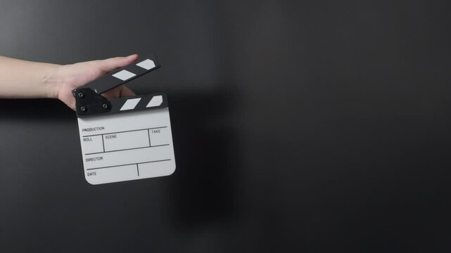 A classic film clapperboard or film slate being held and hit against a dark background. Symbolizes filmmaking video production movie filming and creative storytelling in the entertainment industry.