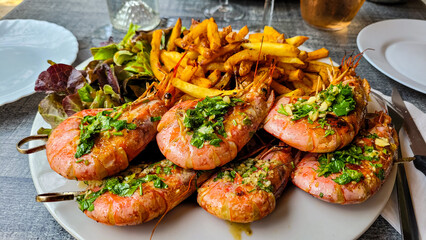 Appetizing and delicious giant red grilled shrimps with parsley and garlic, fried potatoes and salad on a white plate.